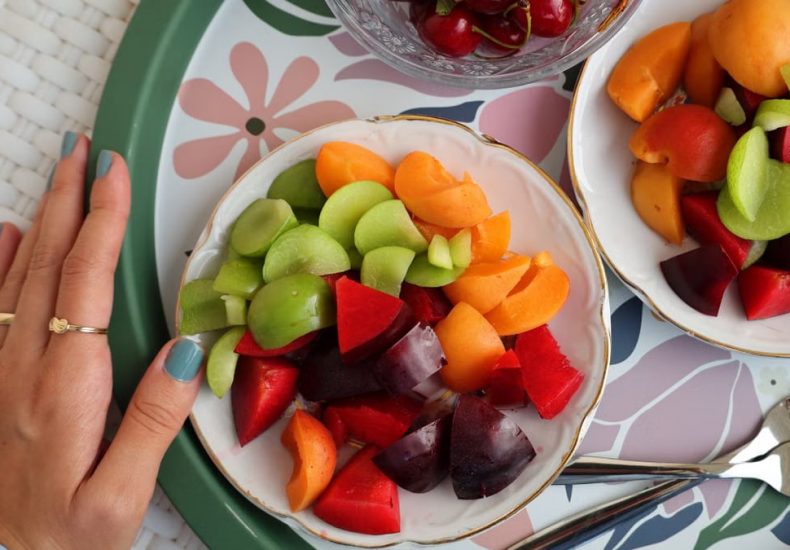 Top view of a colorful fruit platter with cherries, apricots, and plums on a decorative tray.