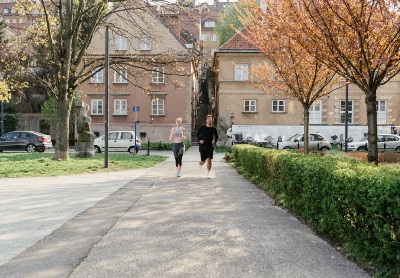 A couple jogging together in an urban park surrounded by greenery and houses.